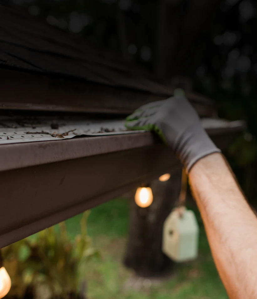 Gloved hand removing debris from gutter