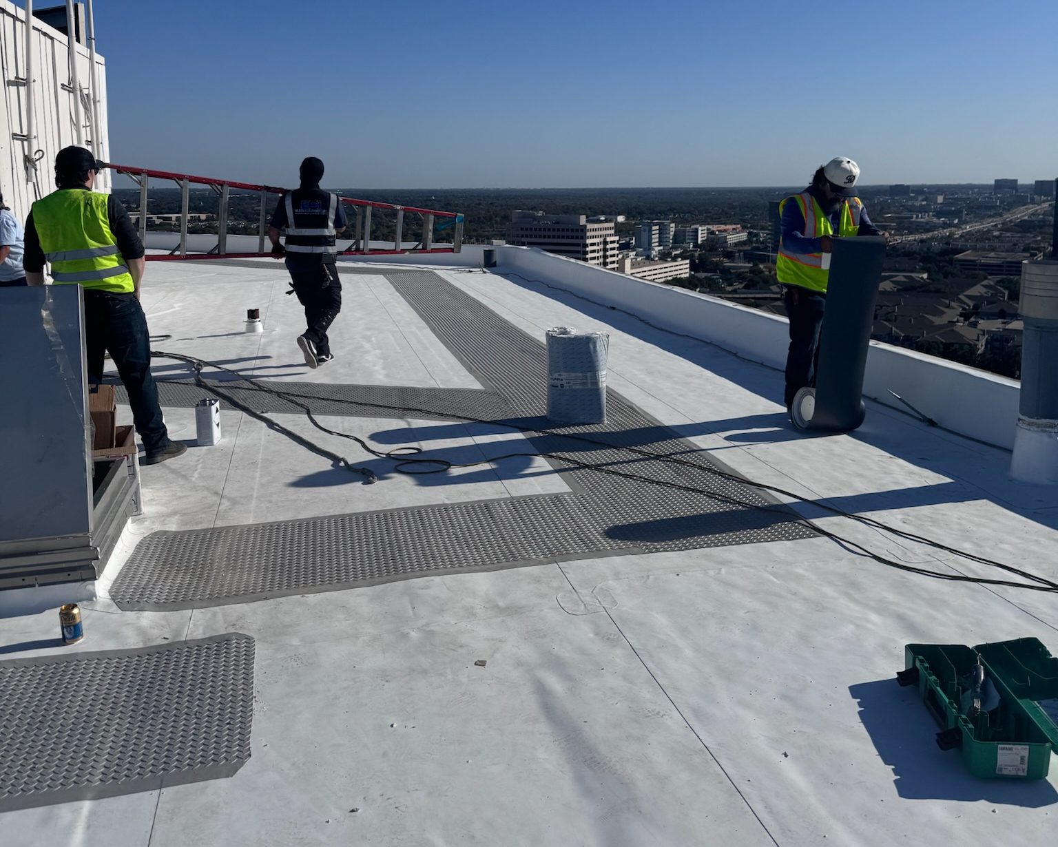 Workers applying a white coating on a flat rooftop under clear skies.